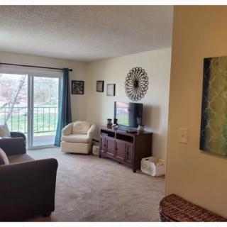 Cozy living room with a sofa, chair, and TV, featuring artwork and a large window for natural light.