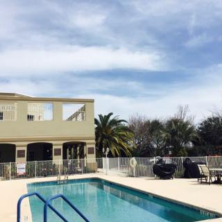 A serene outdoor swimming pool area with palm trees and a building under a clear sky.