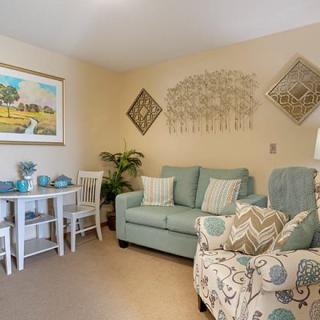 A cozy living room featuring a blue sofa and patterned armchair, complemented by artwork and decorative elements.