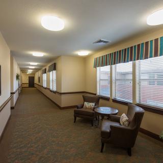 A well-lit hallway with chairs and a small table by the windows.
