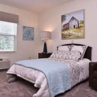 A cozy bedroom with a neatly made bed, featuring artwork on the walls and a lamp on the bedside table.
