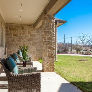 A sunny outdoor patio with wicker chairs and a brick wall overlooking a green lawn.