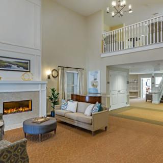 A spacious living room with a modern fireplace, plush sofa, and elegant chandelier under a high ceiling.