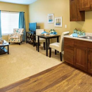 A cozy apartment living room with a kitchenette, featuring warm wooden tones and comfortable furniture.