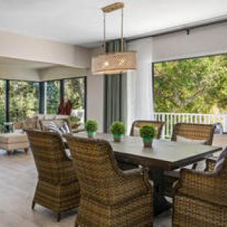 A modern dining room with wicker chairs and a wooden table, surrounded by large windows that let in natural light.