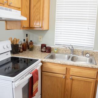 A cozy kitchen with wooden cabinets, a stove, a double sink, and various utensils on the countertop.