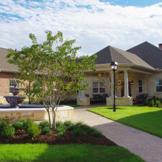 A well-maintained house with a manicured lawn and landscaping featuring a fountain and brick pathway.