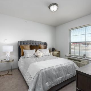 A modern bedroom with a neatly made bed, nightstand, and window.