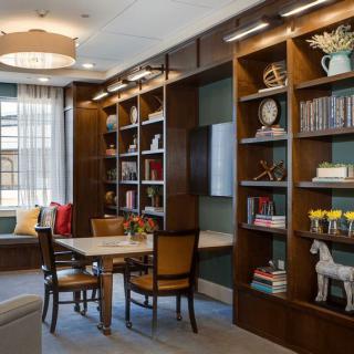 A cozy library room with wooden shelves filled with books, a table and chairs for reading.