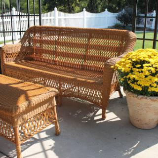 A cozy outdoor seating area featuring a wicker sofa and coffee table, complemented by vibrant yellow flowers in a pot.
