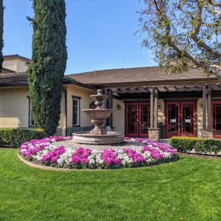 A beautifully landscaped area in front of a building featuring a circular flower bed surrounding a central fountain.