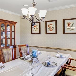 A cozy dining room with a set table, elegant chandelier, and decorative artwork on the walls.