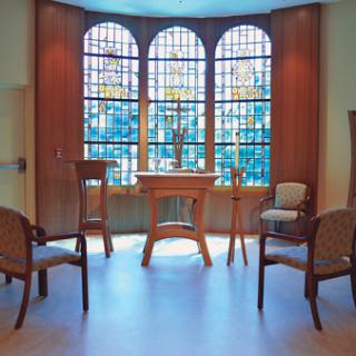 A serene interior featuring stained glass windows and a minimalist setup with chairs and a central table.