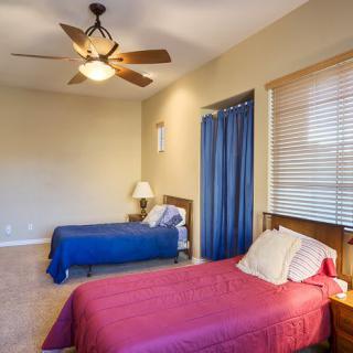 A bedroom with two single beds, a ceiling fan, and window blinds.