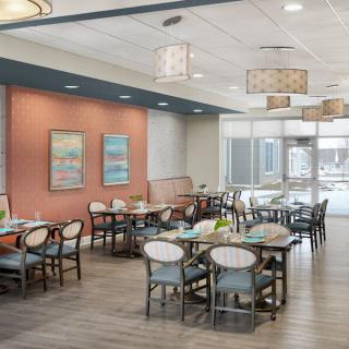 A modern dining area with neatly arranged tables and chairs, featuring stylish lighting fixtures and colorful wall art.