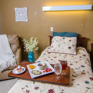 A cozy bedroom setting featuring a neatly made bed, a snack tray with various treats, and a touch of homey decor.