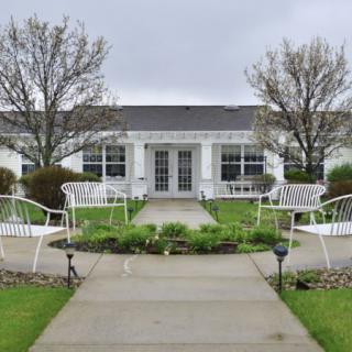 A charming white house with a landscaped garden and pathway, featuring outdoor seating and trees.