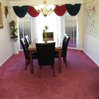 A dining room with a table and chairs, featuring red carpet and decorative curtains.