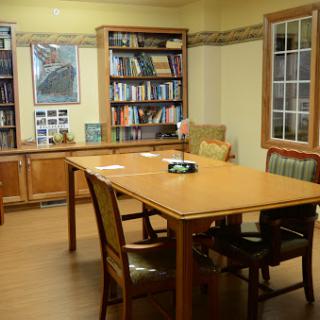 A cozy library meeting room featuring a wooden table, comfortable chairs, and shelves filled with books.