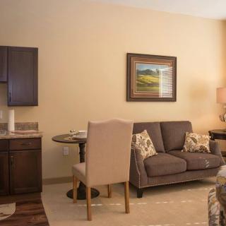 A cozy living room with a sofa, table, and chairs, featuring warm neutral tones and decorative artwork.