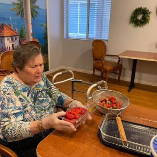 An elderly woman prepares strawberries in a cozy kitchen setting.