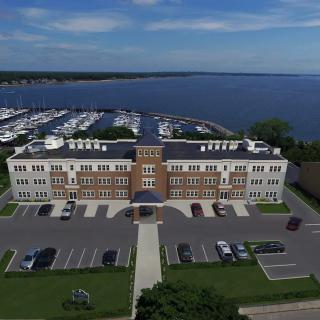 Aerial view of a waterfront building with a parking lot and marina in the background.
