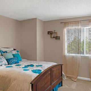 A cozy bedroom with a wooden bed, colorful bedding, and a window with sheer curtains.