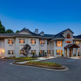 A large residential building with a driveway and landscaped surroundings during the evening.