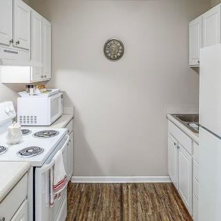 A compact kitchen featuring white appliances and cabinetry with wooden flooring.