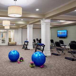 A spacious exercise room equipped with yoga balls, dumbbells, and chairs, featuring a carpeted floor and a television.