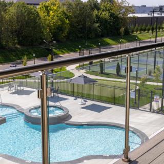 An outdoor recreational area featuring a swimming pool, jacuzzi, and tennis courts surrounded by greenery.
