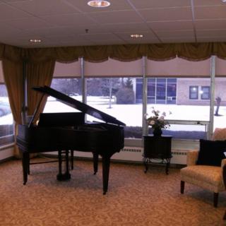 A cozy living room features a grand piano next to large windows with a view of the snowy outdoors.