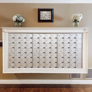 A wall-mounted set of mailboxes in an interior hallway, decorated with flowers and a clock above.