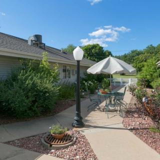 A sunny patio area with a table, chairs, and an umbrella surrounded by lush greenery.