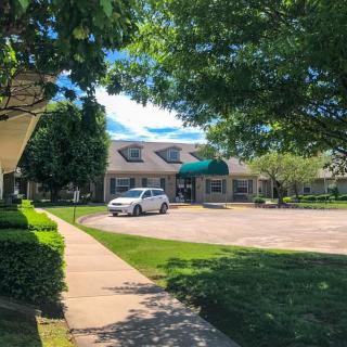A sunny day view of a building with a nearby parking lot and surrounding trees.