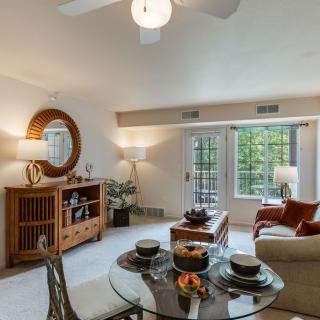 A modern living room featuring a comfortable seating area, a glass dining table, and stylish decor elements next to large windows.