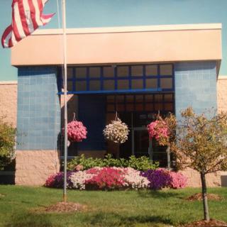 A vibrant building surrounded by blooming flowers and an American flag waving in the foreground.