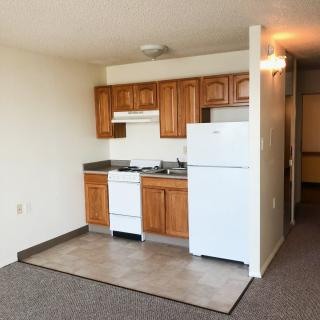 A compact apartment kitchen with wooden cabinets and a white refrigerator.