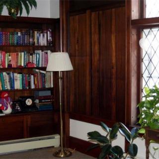 A cozy library nook with a wooden bookshelf filled with books, a floor lamp, and plants by the window.
