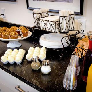 A breakfast buffet with muffins, beverages, and condiments on a countertop.