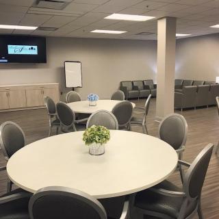 A modern meeting room with round tables, chairs, a television, and a sofa area.