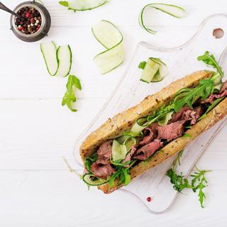 A delicious sandwich filled with meat, fresh greens, and cucumber slices on a wooden board.