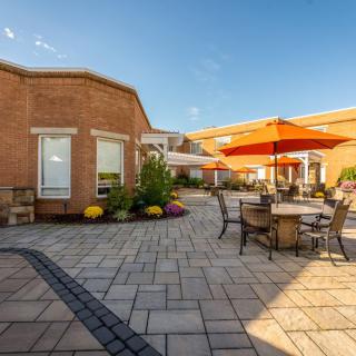 A sunny courtyard with outdoor seating and bright orange umbrellas surrounded by brick buildings.