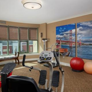 A well-lit gym room featuring a stationary bike, fitness balls, and framed artwork on the wall.