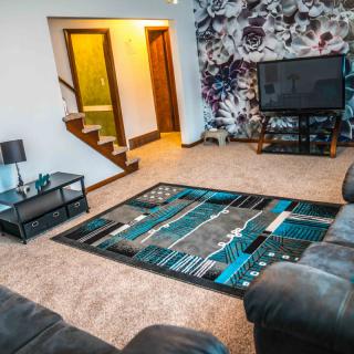 A modern living room featuring a colorful carpet, leather sofas, and a large television.