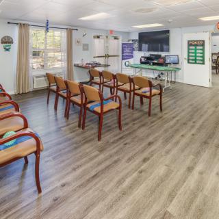 A spacious waiting room with lined-up chairs, wooden flooring, and a large television.