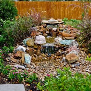A small garden waterfall surrounded by rocks and lush greenery.