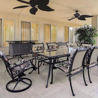 A stylish outdoor patio dining area with a glass table and chairs under ceiling fans.