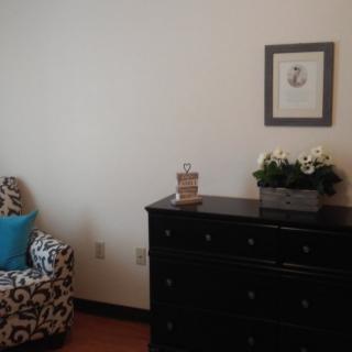 A cozy room with a patterned chair and a dark dresser adorned with decor items.