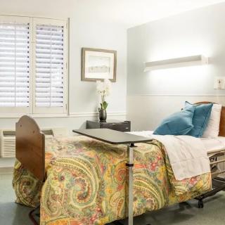 A clean and well-organized hospital room featuring a single bed with colorful bedding.